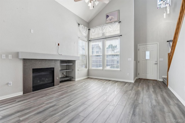 unfurnished living room with light wood-type flooring, ceiling fan, and high vaulted ceiling