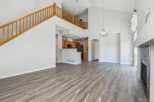 unfurnished living room with light hardwood / wood-style floors, a chandelier, and high vaulted ceiling