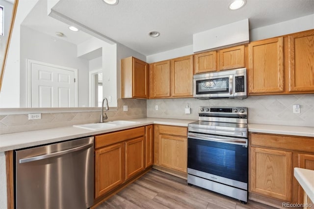 kitchen featuring a textured ceiling, sink, stainless steel appliances, backsplash, and hardwood / wood-style floors