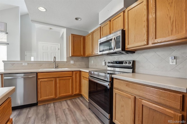 kitchen featuring sink, tasteful backsplash, a textured ceiling, stainless steel appliances, and light wood-type flooring