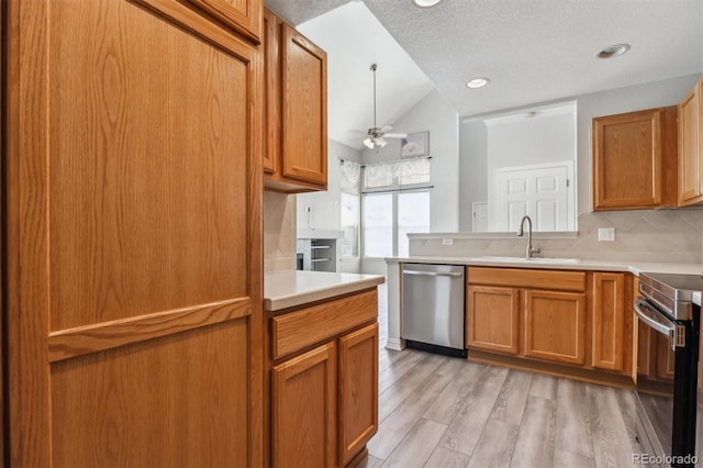 kitchen with appliances with stainless steel finishes, light hardwood / wood-style floors, vaulted ceiling, tasteful backsplash, and sink