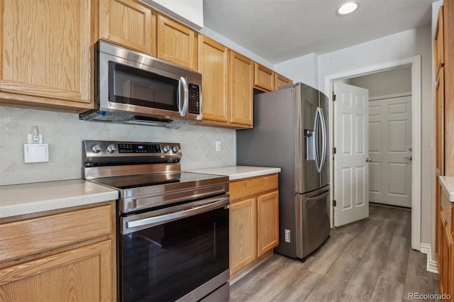 kitchen with a textured ceiling, tasteful backsplash, stainless steel appliances, hardwood / wood-style floors, and light brown cabinetry