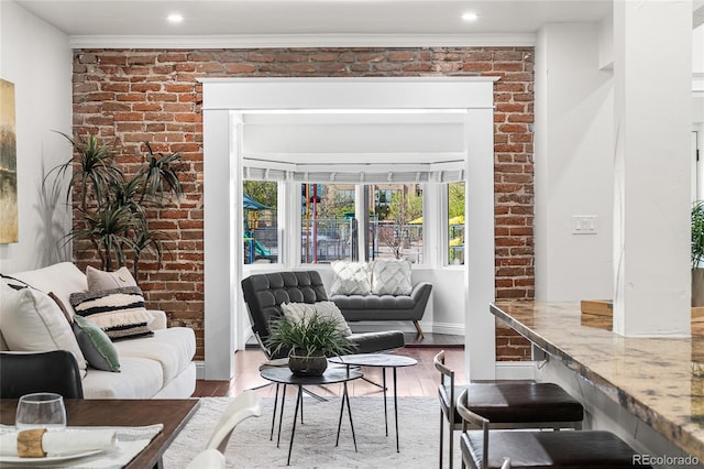 living room featuring wood finished floors, healthy amount of natural light, brick wall, ornamental molding, and baseboards