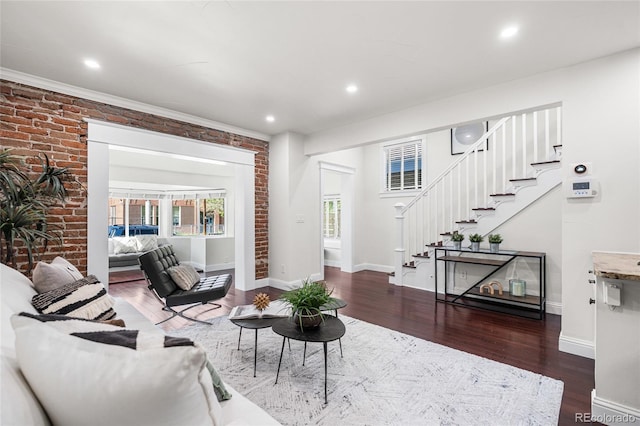 living area with stairway, wood finished floors, baseboards, recessed lighting, and brick wall