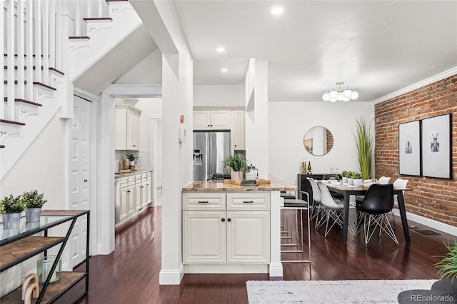 kitchen with stainless steel fridge, brick wall, dark wood-style floors, light stone countertops, and white cabinetry