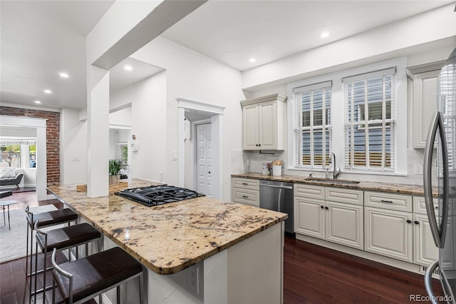 kitchen with a sink, appliances with stainless steel finishes, light stone countertops, a kitchen bar, and recessed lighting