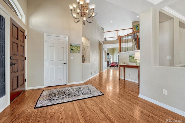 foyer with recessed lighting, a notable chandelier, wood finished floors, a towering ceiling, and baseboards