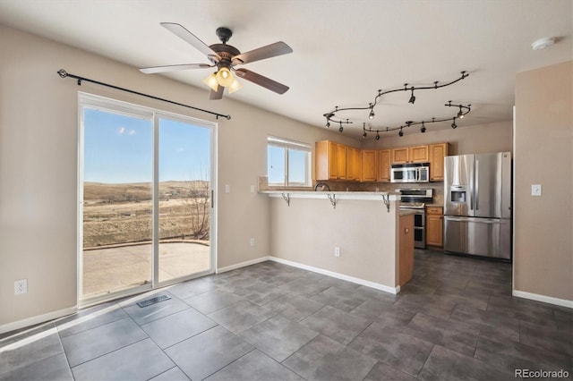 kitchen with appliances with stainless steel finishes, ceiling fan, a kitchen breakfast bar, a peninsula, and baseboards