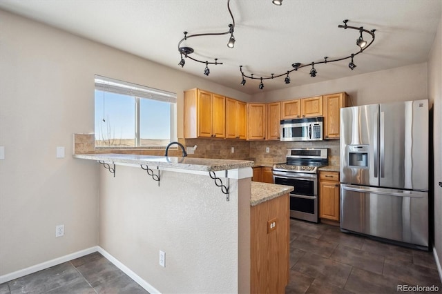 kitchen featuring a breakfast bar area, a peninsula, light countertops, appliances with stainless steel finishes, and decorative backsplash