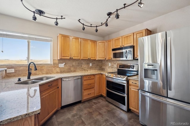 kitchen featuring appliances with stainless steel finishes, a sink, backsplash, and light stone countertops