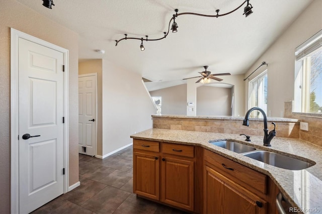 kitchen with a sink, backsplash, light stone countertops, dishwasher, and brown cabinetry