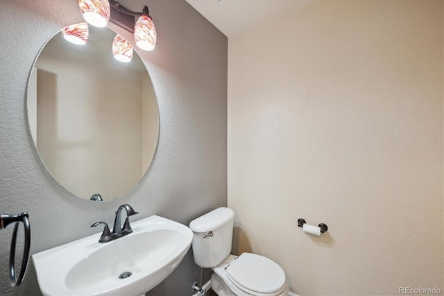 half bath with a textured wall, a sink, and toilet