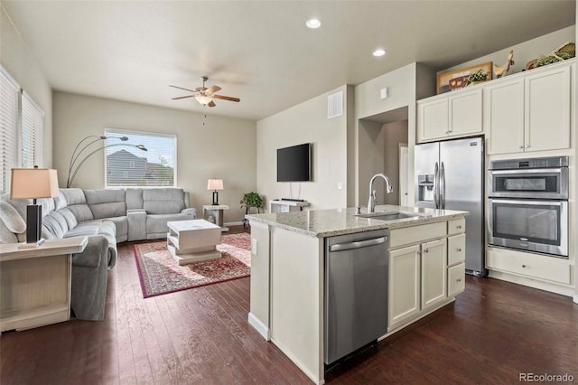 kitchen featuring dark hardwood / wood-style flooring, sink, light stone countertops, appliances with stainless steel finishes, and a center island with sink