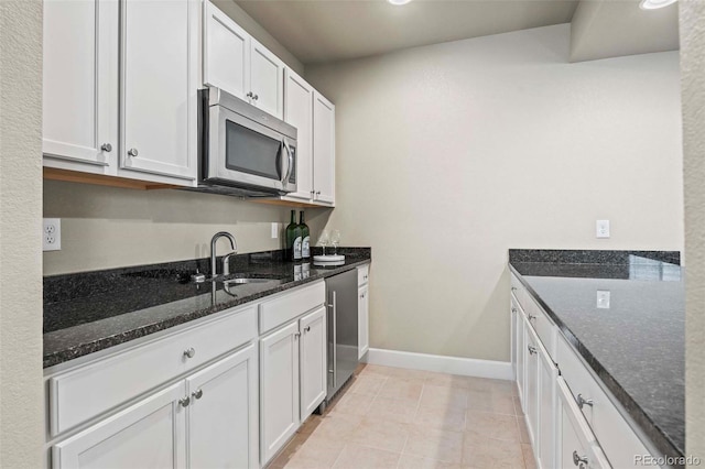 kitchen featuring light tile patterned floors, appliances with stainless steel finishes, white cabinetry, sink, and dark stone counters