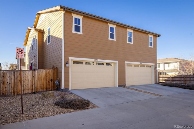 view of side of property with driveway, an attached garage, and fence