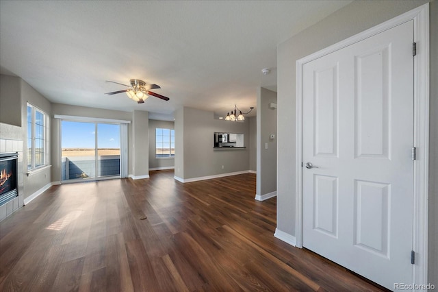 unfurnished living room featuring ceiling fan with notable chandelier, dark hardwood / wood-style flooring, a fireplace, and a water view