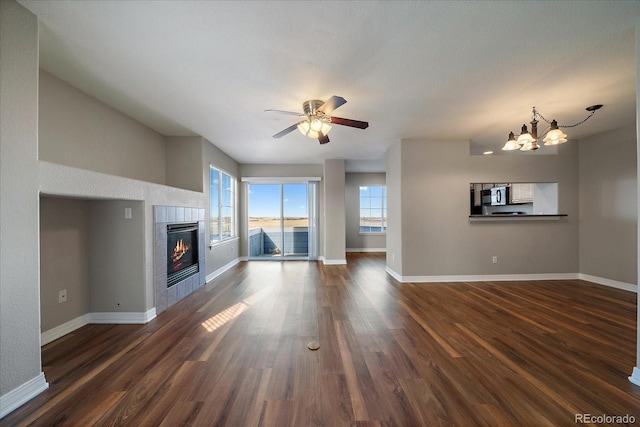 unfurnished living room with a tiled fireplace, dark hardwood / wood-style flooring, and ceiling fan with notable chandelier