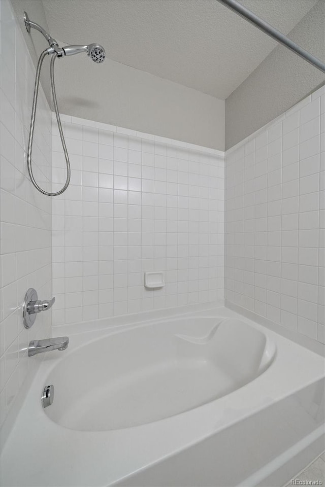 bathroom featuring a textured ceiling and tiled shower / bath