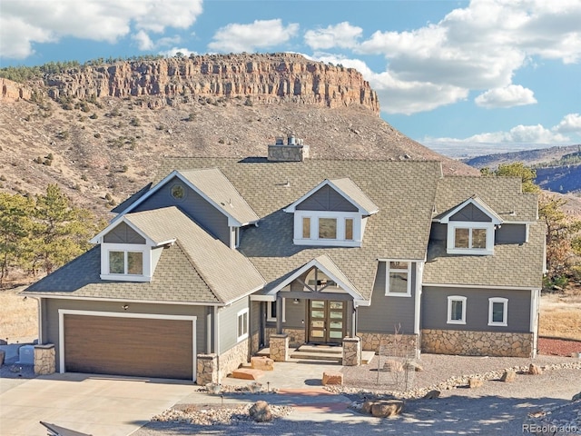 view of front of property with concrete driveway, stone siding, roof with shingles, an attached garage, and french doors