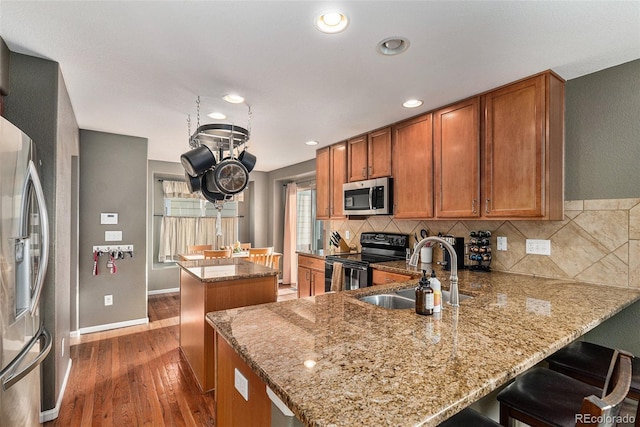 kitchen featuring a sink, a kitchen island, backsplash, stainless steel appliances, and brown cabinetry