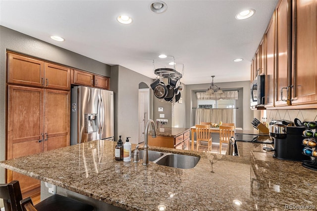 kitchen featuring a peninsula, arched walkways, a sink, appliances with stainless steel finishes, and brown cabinets