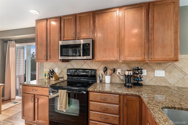 kitchen featuring brown cabinets, stone countertops, stainless steel microwave, tasteful backsplash, and black range with electric cooktop