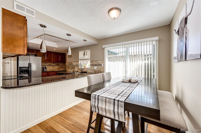 dining area with a textured ceiling, sink, a tray ceiling, and light hardwood / wood-style flooring