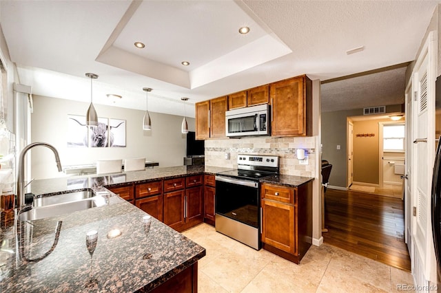 kitchen with pendant lighting, dark stone counters, sink, a tray ceiling, and stainless steel appliances