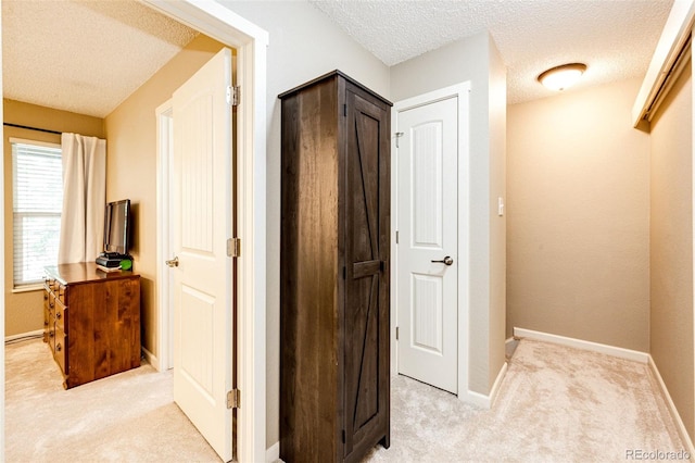 hallway with a textured ceiling and light colored carpet