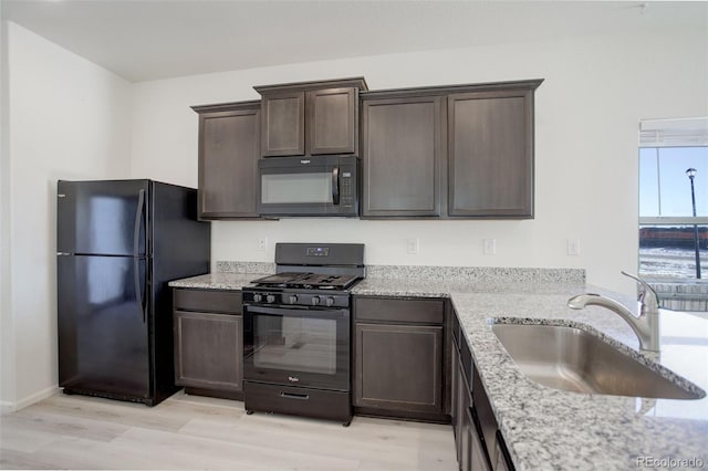 kitchen with dark brown cabinetry, sink, black appliances, and light hardwood / wood-style floors