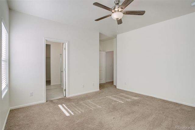 unfurnished bedroom with light carpet, a walk in closet, and ceiling fan