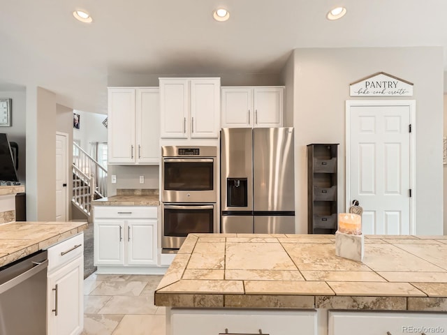 8010 Raspberry Dr, Frederick, CO 80504 - kitchen featuring appliances with stainless steel finishes, white cabinetry, recessed lighting, light marble finish flooring, and tile countertops