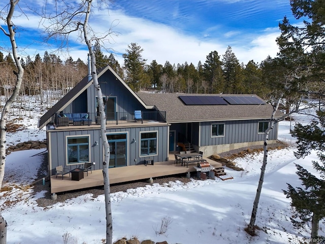 snow covered back of property with a wooden deck, a balcony, and solar panels