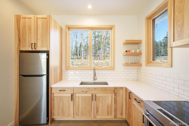 kitchen featuring light brown cabinets, sink, stainless steel fridge, tasteful backsplash, and range