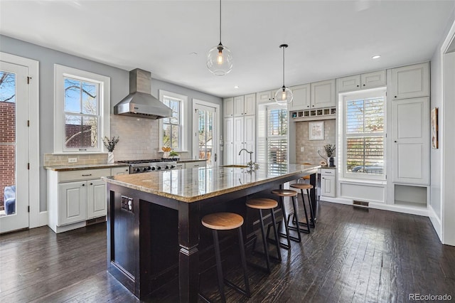 201 S Lafayette St, Denver, CO 80209 - kitchen featuring wall chimney exhaust hood, dark wood-style floors, light stone countertops, tasteful backsplash, and pendant lighting