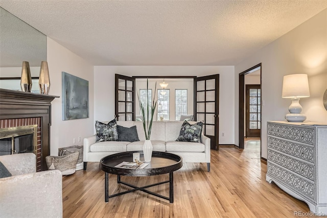 living room with light wood-style floors, a fireplace, baseboards, and a textured ceiling