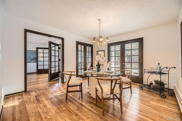 dining area with light wood-style flooring, baseboard heating, a textured ceiling, french doors, and a chandelier