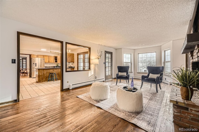 living area featuring light wood-type flooring, a baseboard radiator, and a textured ceiling