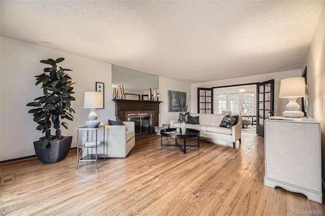 living room featuring a brick fireplace, light wood-style flooring, visible vents, and a textured ceiling