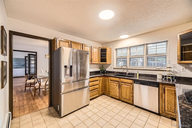 kitchen featuring stainless steel appliances, baseboard heating, brown cabinetry, light tile patterned flooring, and a sink