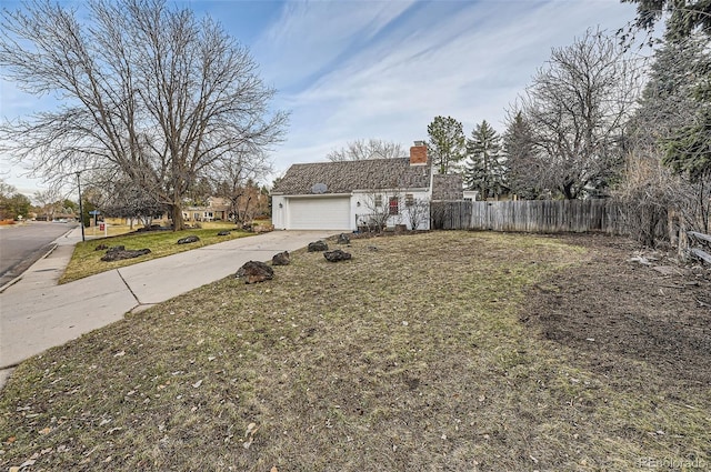 exterior space with an attached garage, fence, concrete driveway, a yard, and a chimney