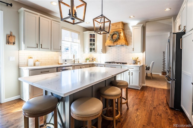 kitchen with white cabinetry, a center island, decorative light fixtures, custom range hood, and appliances with stainless steel finishes