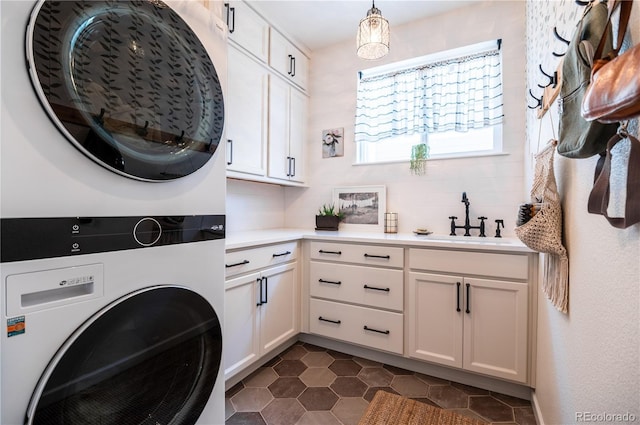 laundry area with cabinets, stacked washing maching and dryer, sink, and dark tile patterned floors