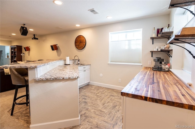 kitchen with a breakfast bar area, light parquet flooring, kitchen peninsula, and white cabinets