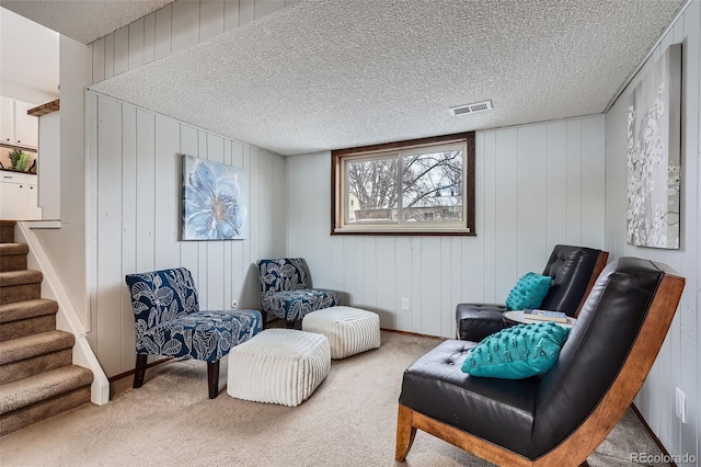 living area with light colored carpet, a textured ceiling, and wood walls