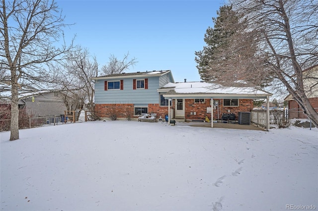 snow covered back of property with covered porch and central AC unit