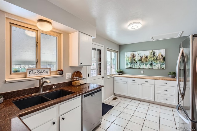 kitchen with appliances with stainless steel finishes, white cabinetry, dark stone counters, sink, and light tile patterned flooring