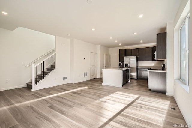 kitchen featuring sink, light wood-type flooring, an island with sink, appliances with stainless steel finishes, and dark brown cabinets