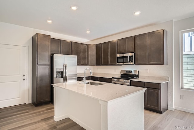 kitchen featuring dark brown cabinetry, stainless steel appliances, a kitchen island with sink, sink, and light hardwood / wood-style floors