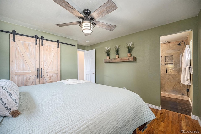 bedroom featuring hardwood / wood-style floors, ensuite bath, a barn door, and ceiling fan